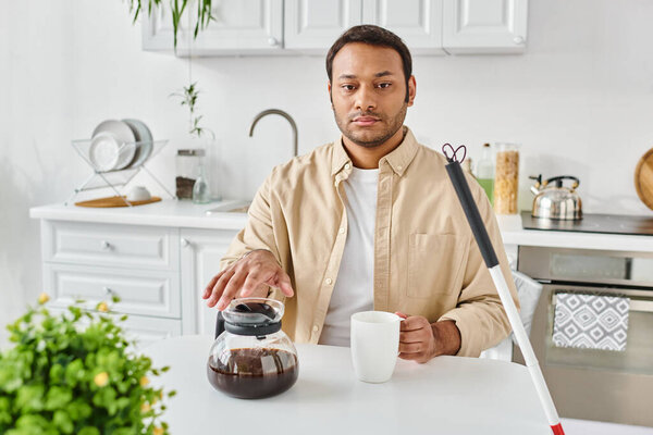 indian blind handsome man in casual attire with walking stick sitting and pouring himself coffee