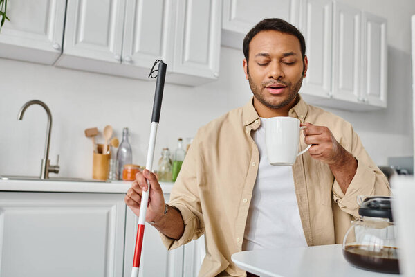 attractive indian man with visual impairment sitting and drinking tasty coffee while on kitchen