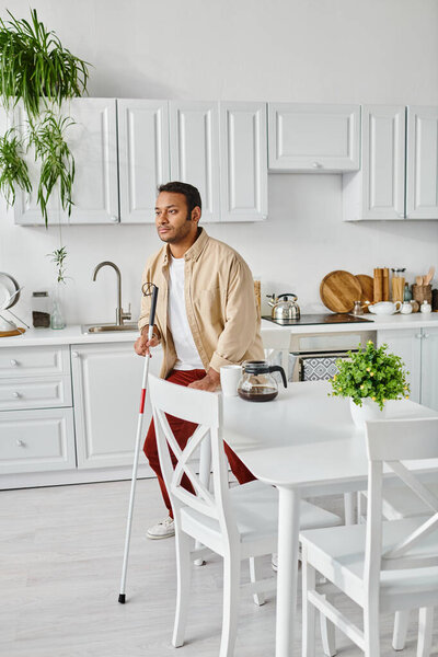 good looking disabled indian man in cozy homewear with walking stick holding coffee cup on kitchen