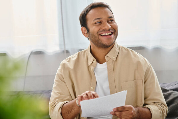 cheerful indian blind man in casual comfortable attire sitting on sofa and reading braille code