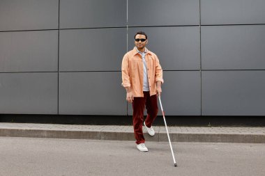 attractive indian man with blindness in jacket with glasses and stick with gray wall on backdrop clipart