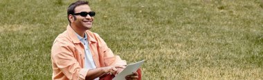 Ceketli mutlu Hintli kör adam çimenlerde oturmuş, gözlüklü ve körler alfabesi, afiş okuyor.