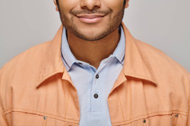 cropped view of cheerful indian man in orange jacket posing on gray backdrop and smiling happily clipart