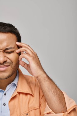 good looking indian man in orange vibrant jacket suffering from headache on gray background clipart