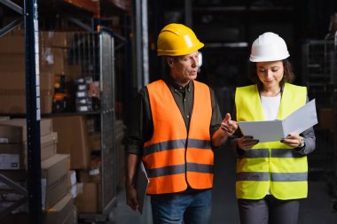 colleagues in safety vests walking in a well-lit warehouse and planning their work, logistic clipart
