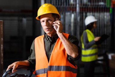 Depo amiri arka planda bayan bir meslektaşıyla akıllı telefondan bir telefon görüşmesi yapıyor.