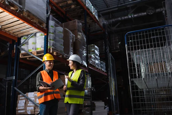 stock image happy professionals in hard hats talking in a warehouse, middle aged boss and subordinate