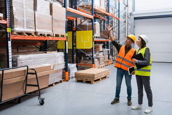 cheerful supervisor with tablet pointing out details to female employee in a warehouse with cargo