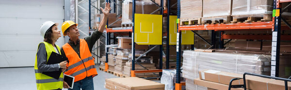 banner of happy supervisor pointing out details to female employee in a warehouse with cargo