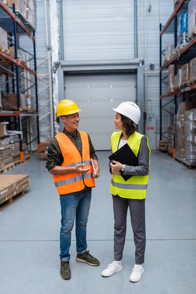 Warehouse employees having a friendly chat, happy man and woman in hard hats and safety vests