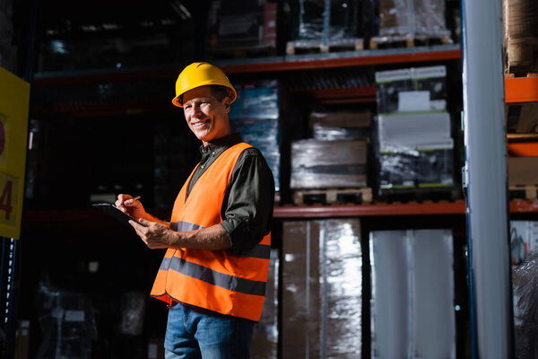 happy middle aged warehouse supervisor in hard hat with clipboard, professional headshots