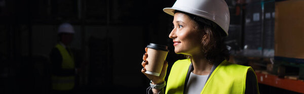 banner of happy woman in hard hat holding paper cup, warehouse employee during coffee break