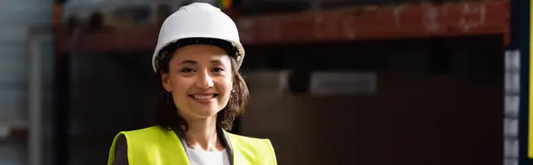 stock image banner of professional woman in safety vest and hard hat standing with hands in pockets in warehouse