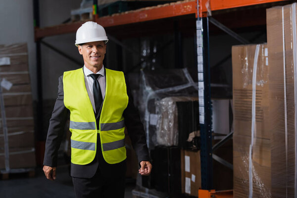 Smiling man in safety vest and hard hat and safety vest walking in warehouse, professional headshot