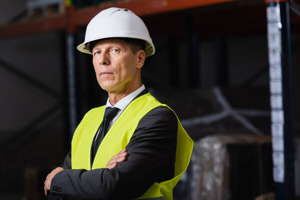 confident man in safety vest and hard hat standing with arms crossed, professional headshot