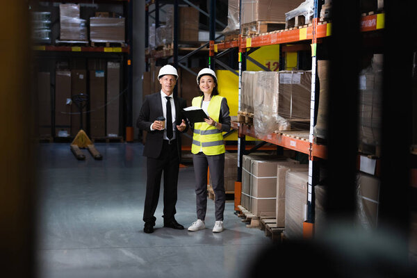 smiling businessman in suit and hard hat discussing logistics operations with female employee