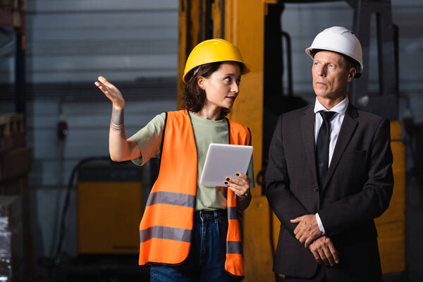 business meeting in a warehouse, female employee with tablet showing something to supervisor in suit
