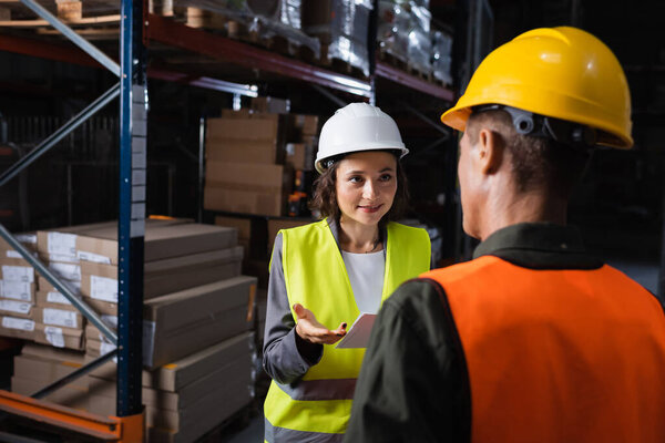 warehouse workers discussing logistics, cheerful woman with folder looking at middle aged colleague