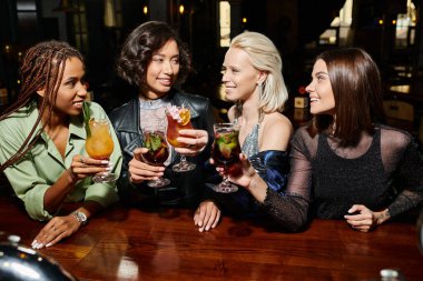 Barda kokteyl bardakları tutan neşeli çoklu etnik kadınlar, dost canlısı atmosferde eğlence.