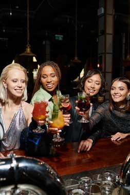 hen party in bar, young multiracial fashionistas smiling and toasting with glasses of cocktails clipart