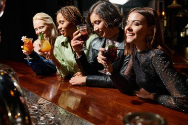Gece partisinde bar tezgahının yanında lezzetli kokteylleri olan çok kültürlü genç kadınlar.