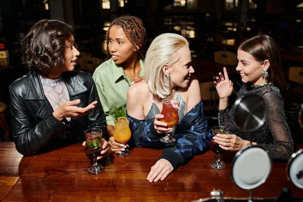 cheerful multiracial female friends with cocktail glasses talking in bar, leisure and party time
