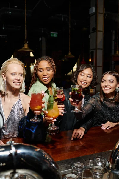 hen party in bar, young multiracial fashionistas smiling and toasting with glasses of cocktails