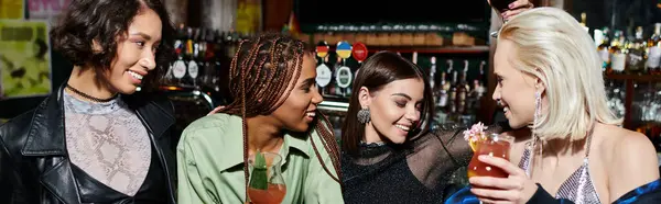 happy multicultural female friends holding cocktails during conversation in bar, horizontal banner