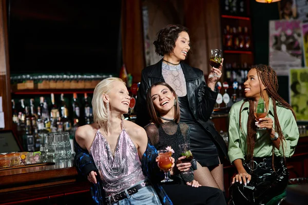 fashionable multiracial female friends with cocktail glasses spending time in modern bar, leisure