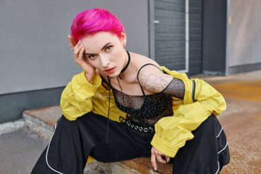 Pembe saçlı ve dövmeli şık, çekici bir kadın kameraya, modaya bakıyor.