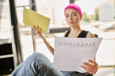Bulanık pembe saçlı kadın günlük giysiler içinde kitap okuyor ve iflasını bildiriyor.