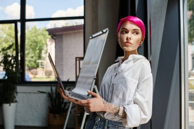 Diz üstü bilgisayarı olan pembe saçlı, düşünceli bir kadın. Ofise bakmıyor, iş konseptine bakmıyor.