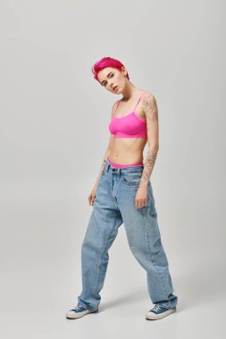 Çekici pembe saçlı kadın manken pembe bluzlu ve kot pantolonlu kameraya bakıyor ve poz veriyor.