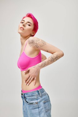 Çekici, pembe saçlı, dövmeli, poz veren ve kameraya bakan genç bir manken.