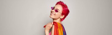 Genç memnun kadın aktivist pembe saçlı ve güneş gözlüklü lgbt gökkuşağı bayrağı ile poz veriyor.