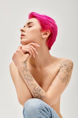 Kadın zarafeti, büyüleyici üstsüz kadın pembe saçlı gri arka planda kot pantolon giymiş.