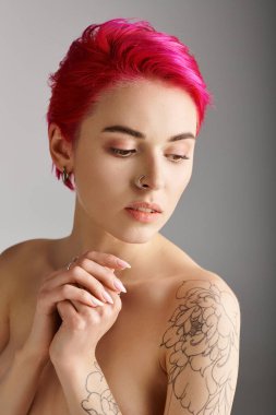 Gri arka planda çıplak omuzları ve dövmesi olan çekici ve üstsüz genç bir kadının portresi.