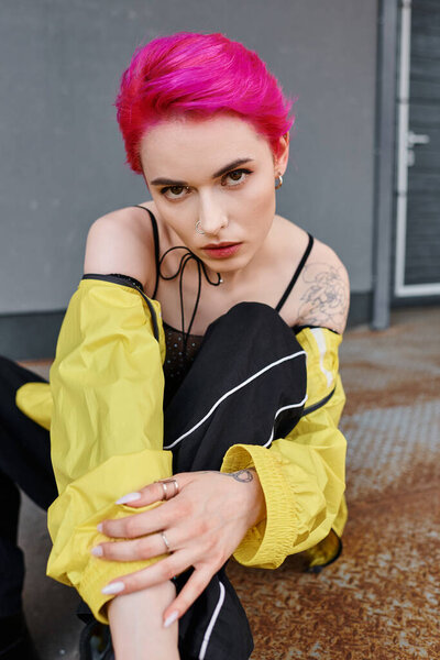 appealing fashionable woman in vibrant urban attire sitting and looking at camera, fashion concept