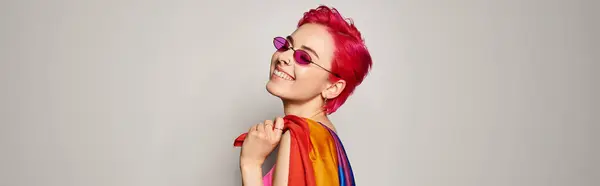 young pleased female activist with pink hair and sunglasses posing with lgbt rainbow flag, banner