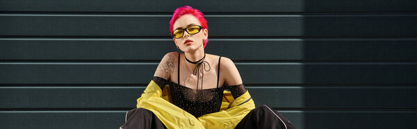 young woman with pink hair and tattoo posing in yellow sunglasses and stylish attire, banner