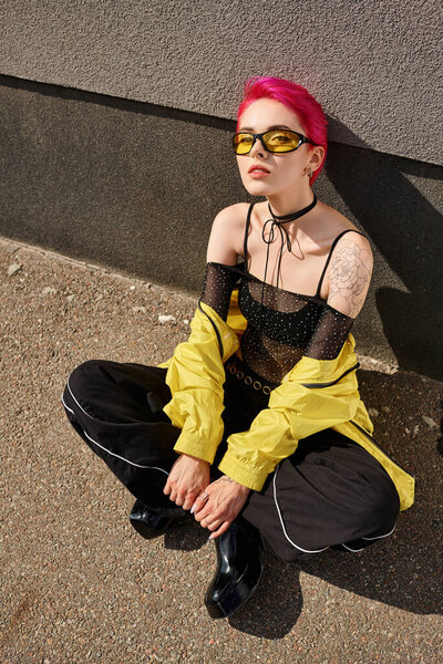 над головой, розовые волосы молодая женщина в солнцезащитных очках и модный наряд позируя при взгляде на камеру