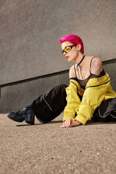 full length, pink haired woman in yellow sunglasses and trendy outfit posing on street. chic look
