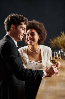 Neşeli Afrikalı Amerikalı kadın elinde şarap kadehiyle sevgililer gününde bir erkeğe bakıyor.