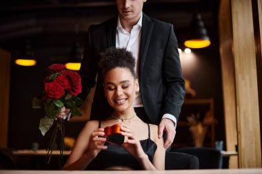 Sevgililer Günü 'nde elinde kalp şeklinde bir kutu tutan mutlu Afrikalı Amerikalı kadına kırmızı güller hediye eden bir adam.