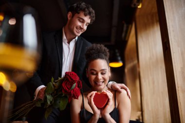 Sevgililer Günü 'nde kalp şeklinde kutuları olan Afrikalı Amerikalı genç bir kadının yanında kırmızı güller tutan bir adam.