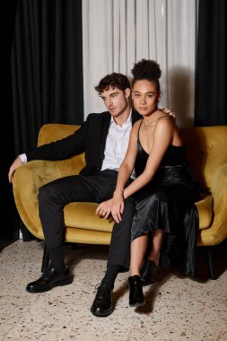 Güzel Afro-Amerikalı kadın, kadife koltukta siyah takım elbiseli yakışıklı bir adamın yanında oturuyor.