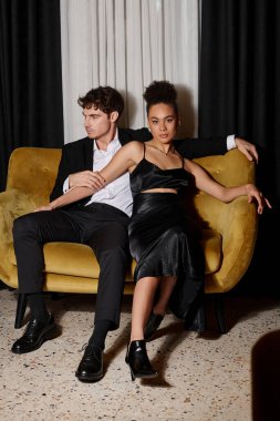 Çekici Afro-Amerikalı kadın kadife koltukta siyah takım elbiseli yakışıklı bir adamın yanında oturuyor.