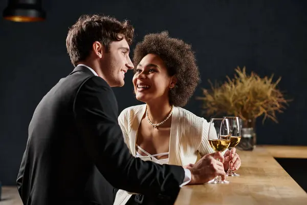 Neşeli Afrikalı Amerikalı kadın elinde şarap kadehiyle sevgililer gününde bir adama bakıyor.