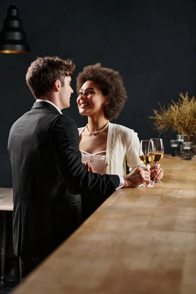 happy african american lady holding wine glass and looking at man during date on valentines day