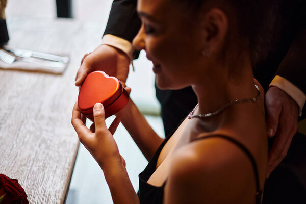 young man gifting heart-shaped box to happy african american girlfriend on Valentines day